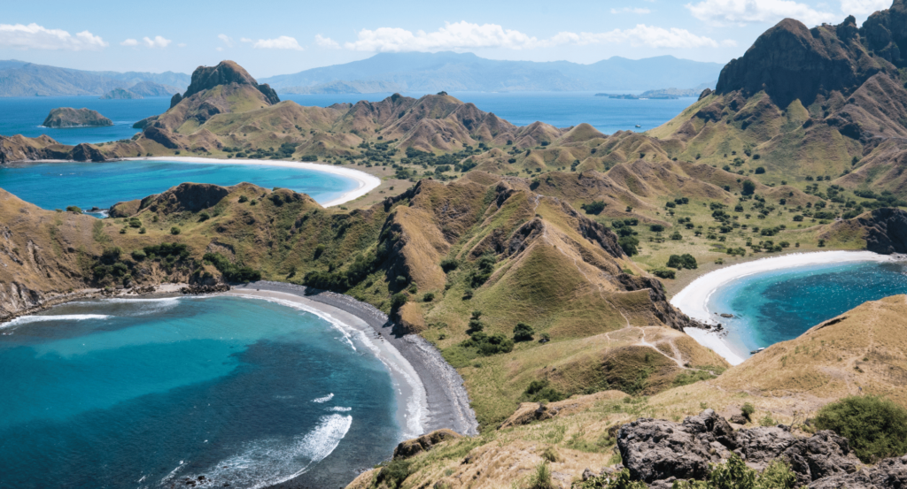 Pemandangan spektakuler dari puncak Pulau Padar dengan teluk-teluk berwarna biru, hijau, dan cokelat. 