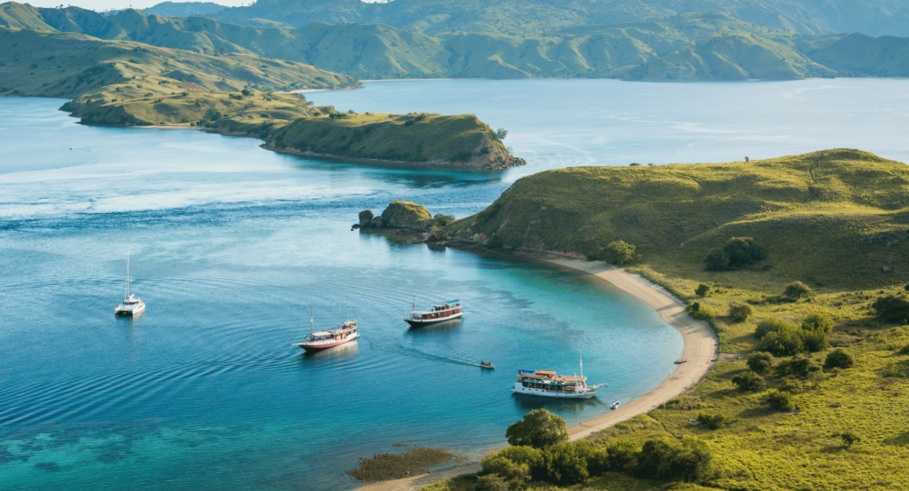 Pemandangan Gili Lawa yang menakjubkan, menampilkan laut biru, pulau hijau, dan beberapa kapal berlabuh di sekitarnya. 