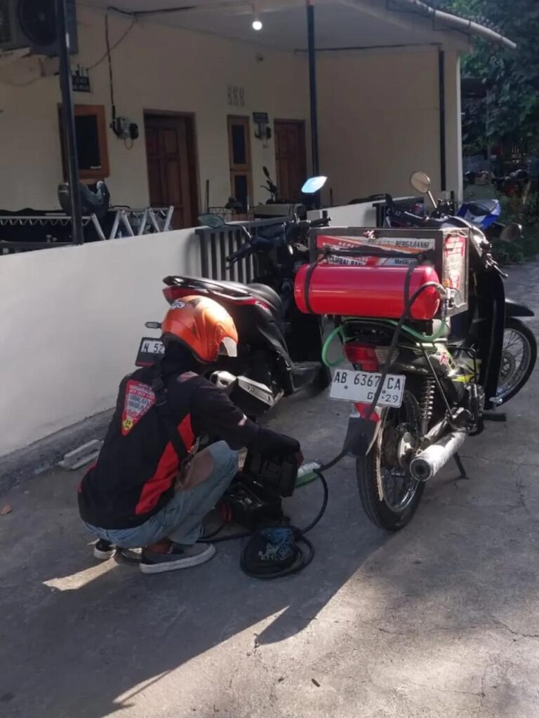Teknisi tambal ban online sedang memperbaiki ban motor di pinggir jalan